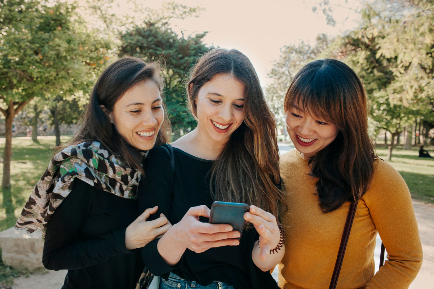 young women outside in a park looking at a phone